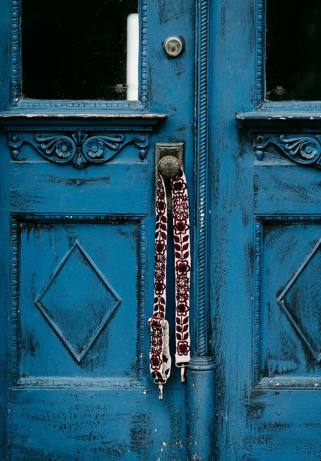 Wendi Adjustable Strap displayed hanging around the doorknob of a blue antique door.
