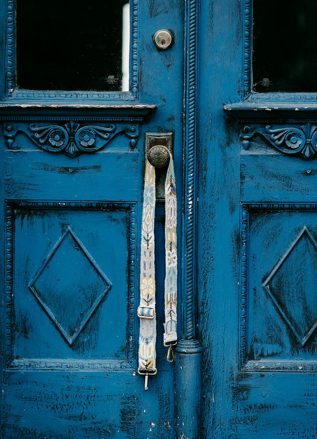 The Yellow Adjustable Purse Strap hanging on doorknob of an antique blue door