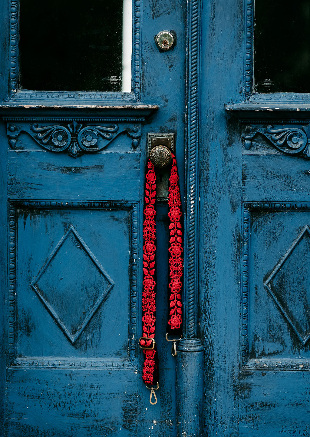 Kennedi Adjustable Strap hanging on doorknob of an antique blue door
