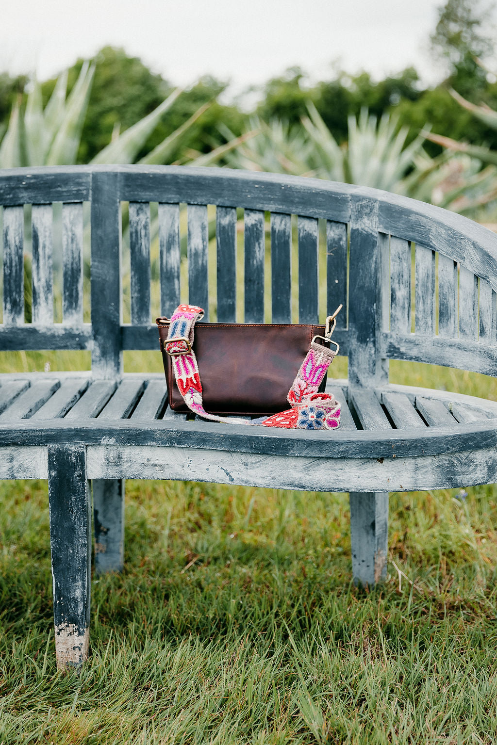 A brown leather purse with a colorful strap displayed on a bench