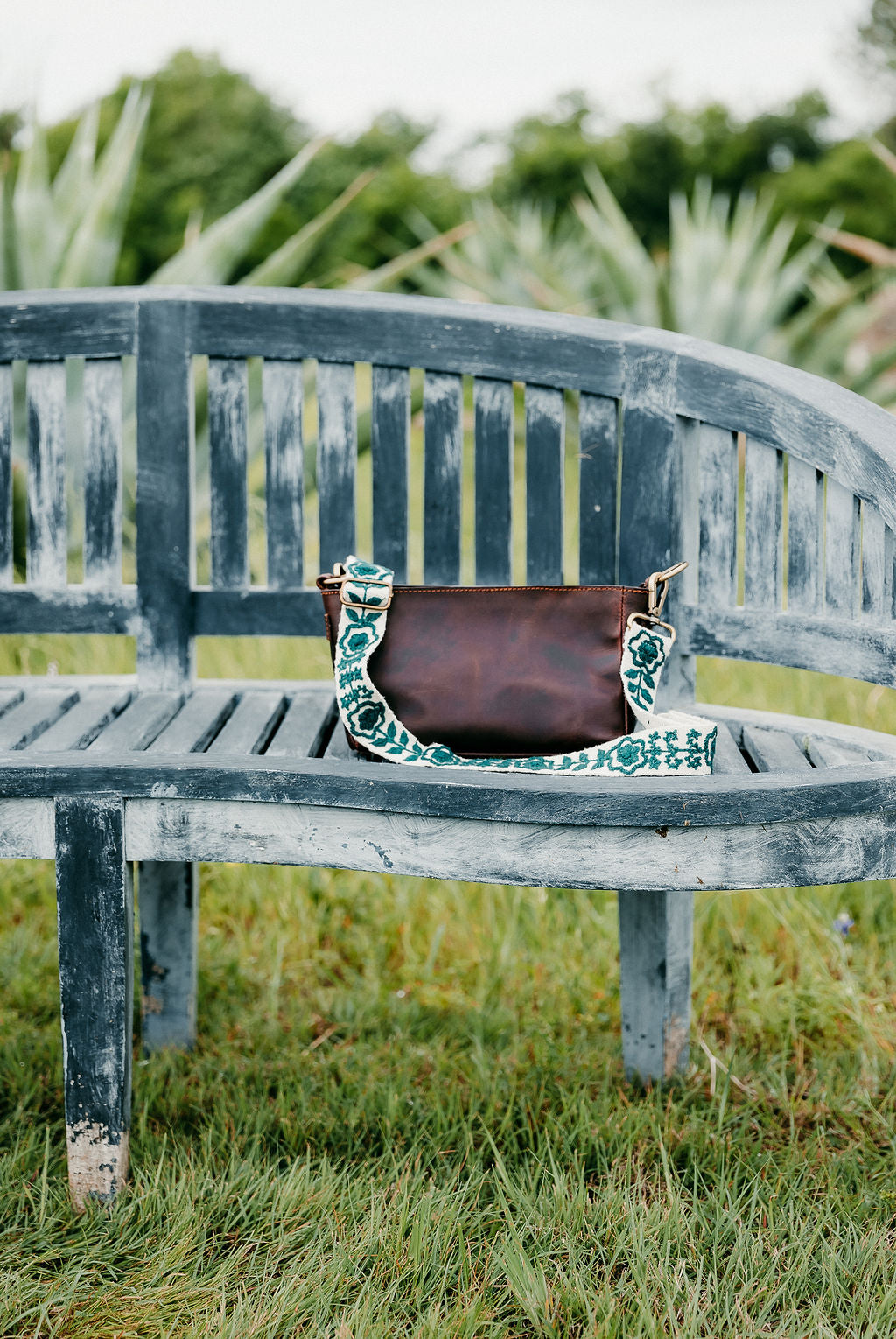 Jill Adjustable Strap attached to brown leather purse displayed on a bench.