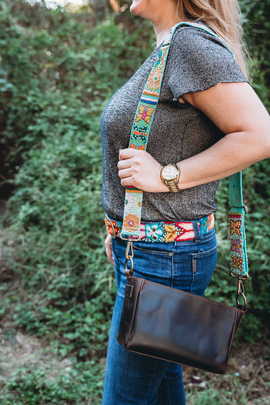 A woman wearing the butterfly adjustable strap purse attached to a brown leather fair trade purse in an outdoor setting.