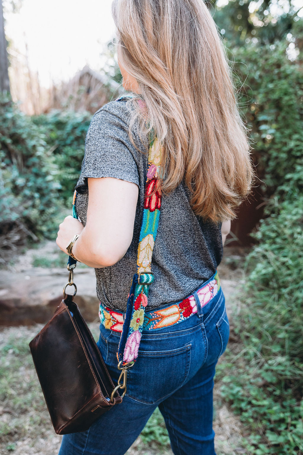A woman wearing the Navy Floral Adjustable Strap attached to a fair trade brown leather purse.
