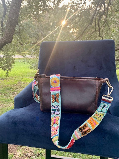 Butterfly Adjustable strap attached to a brown leather purse displayed on a chair outside at sunset.